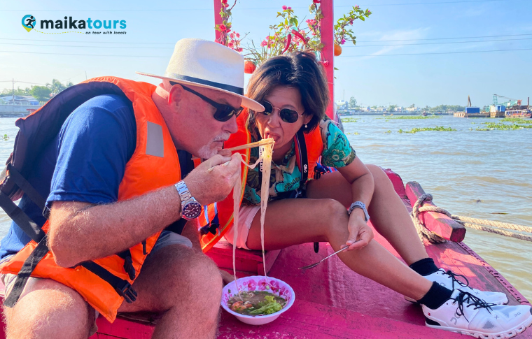 a couple eating hu tieu on a moving boat